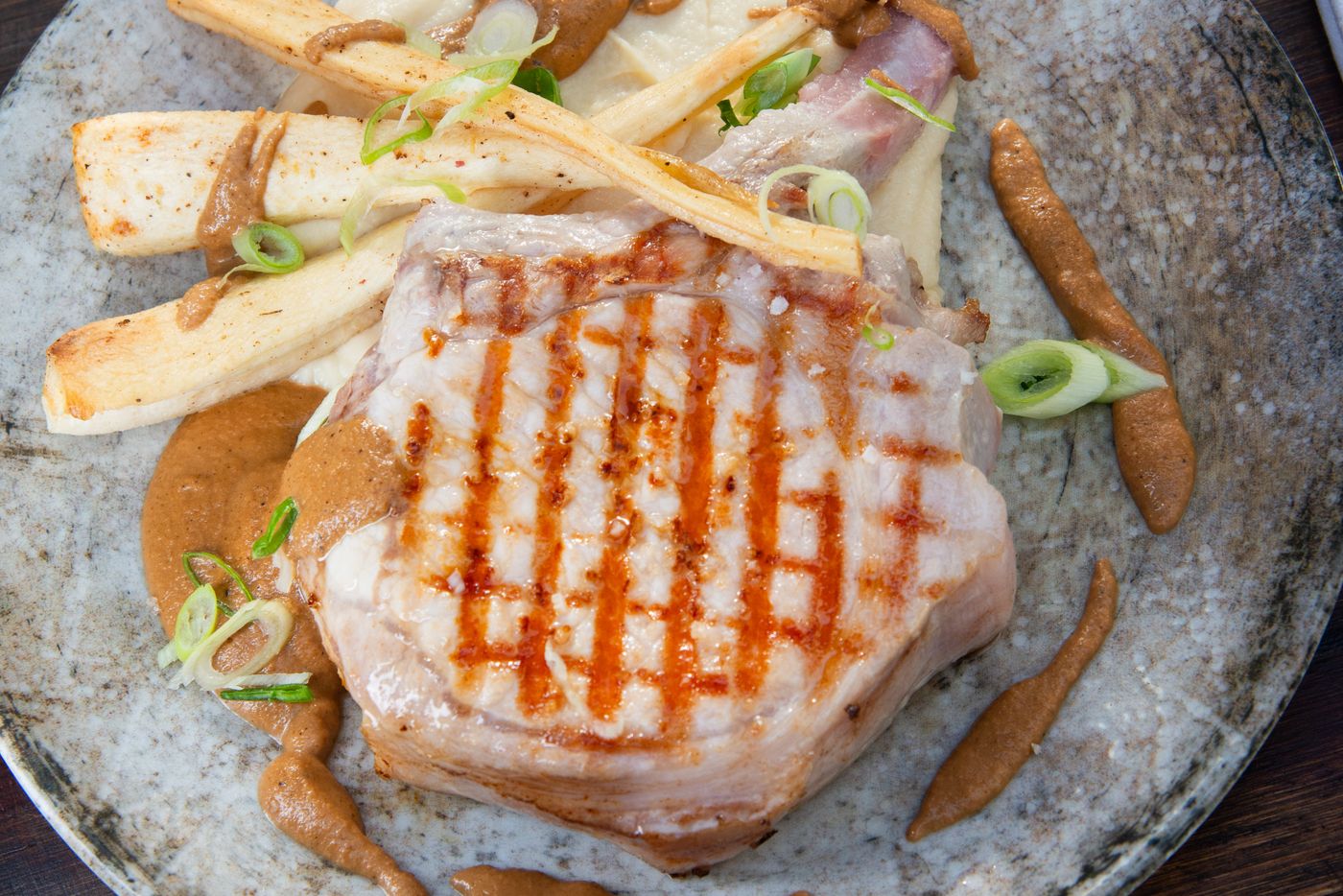 Côte de porc grillée, sauce noisette, panais rôtis et oignons nouveaux, servie dans le grès bleu Chez Benoît