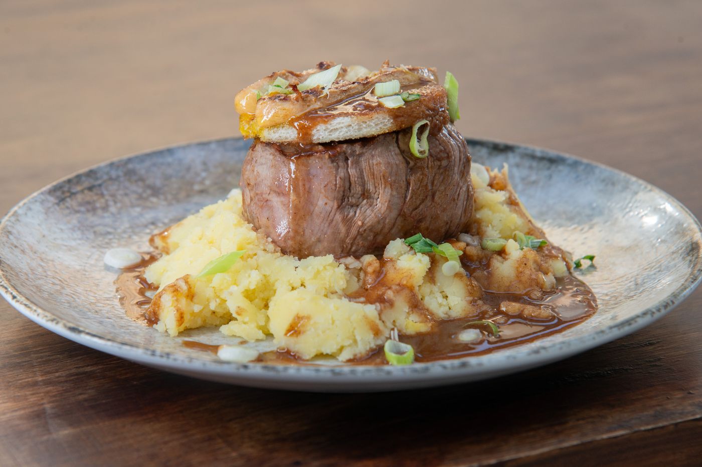 Tournedos de bœuf sur un écrasé de pommes de terre, sauce brune, servi dans une assiette en grès bleu Chez Benoît